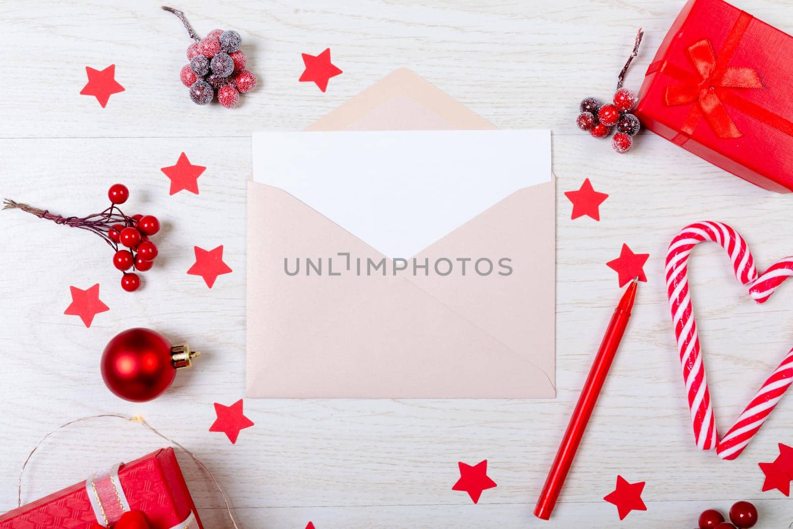 Composition of christmas decorations with envelope and red stars on white wooden background. christmas, tradition and celebration concept.