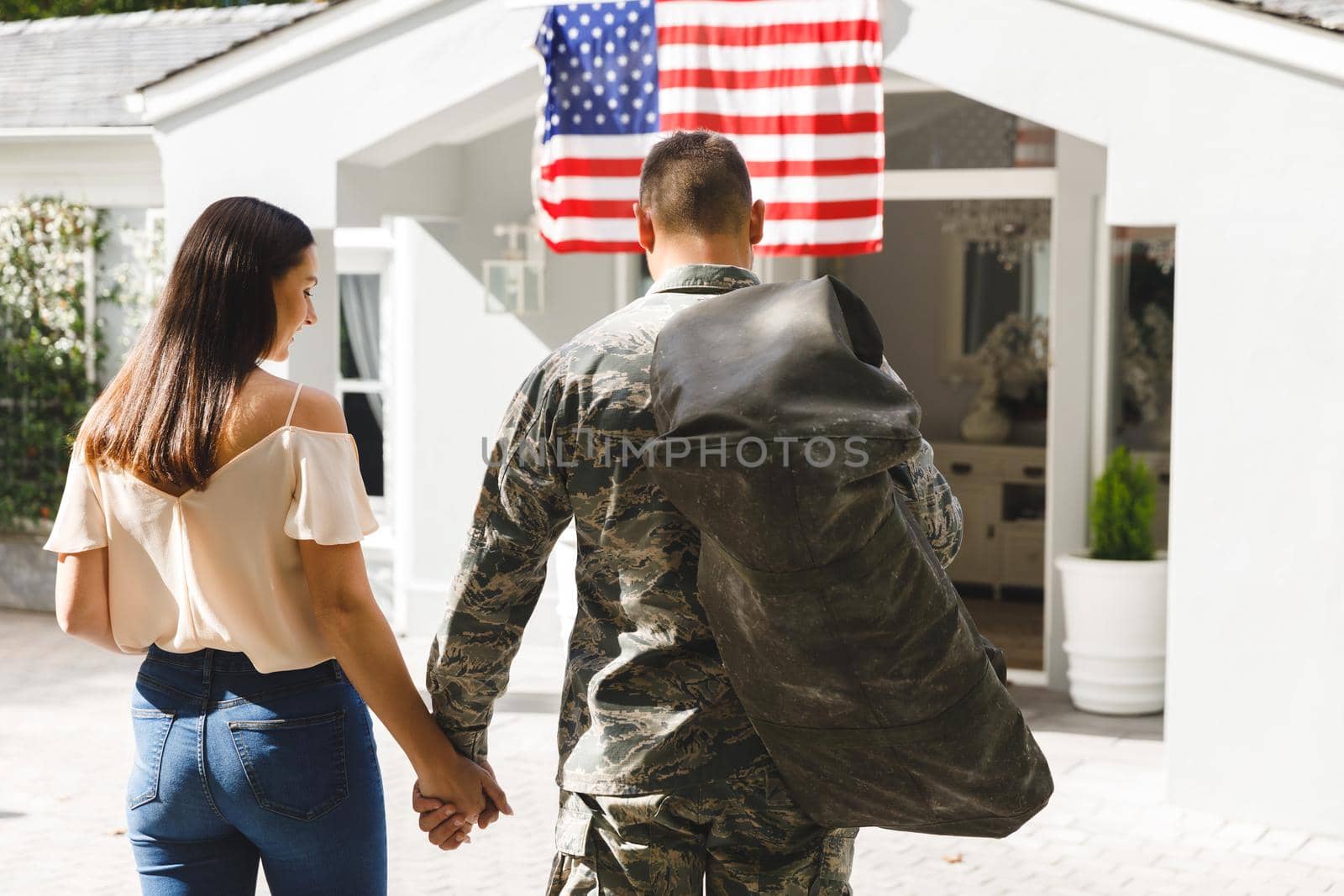 Caucasian male soldier holding hands with wife outside house decorated with american flag. soldier returning home.