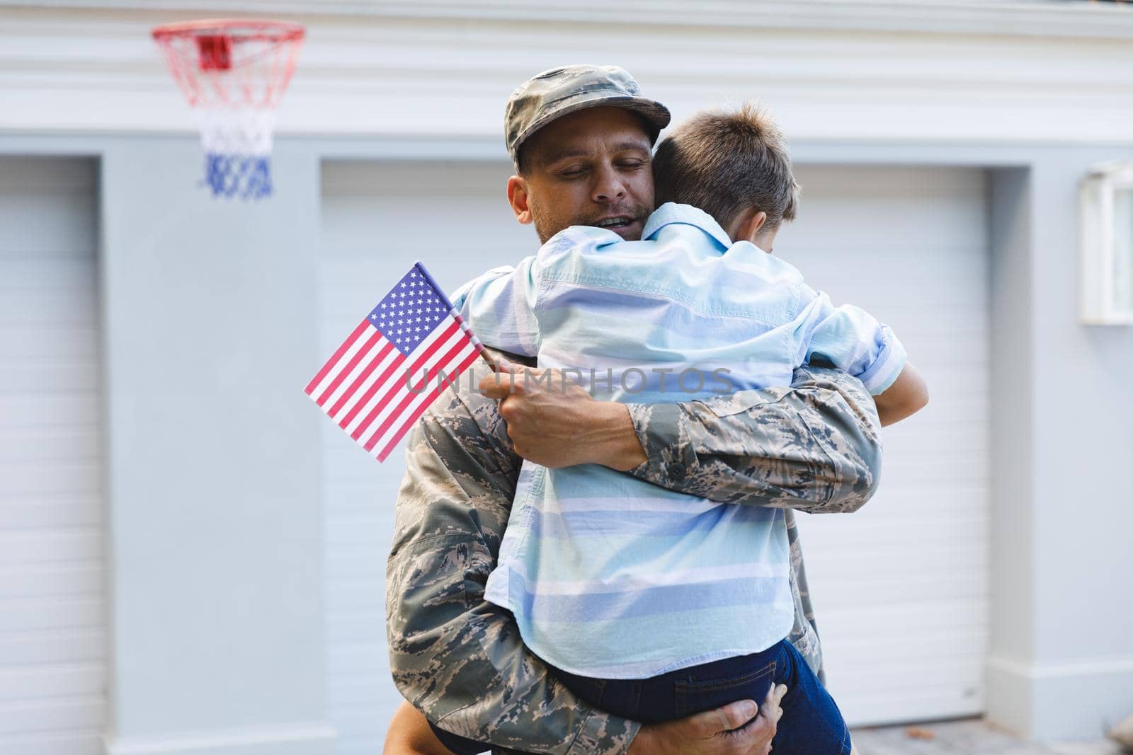 Smiling caucasian male soldier with son outside house holding american flags by Wavebreakmedia