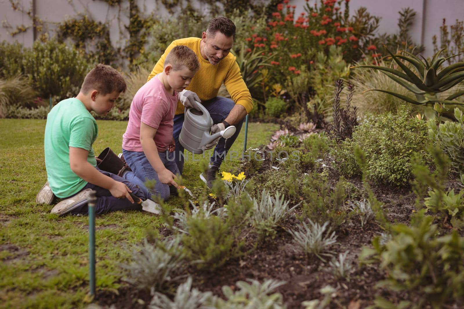 Caucasian father and two sons watering plants together in the garden. fatherhood and gardening hobby concept