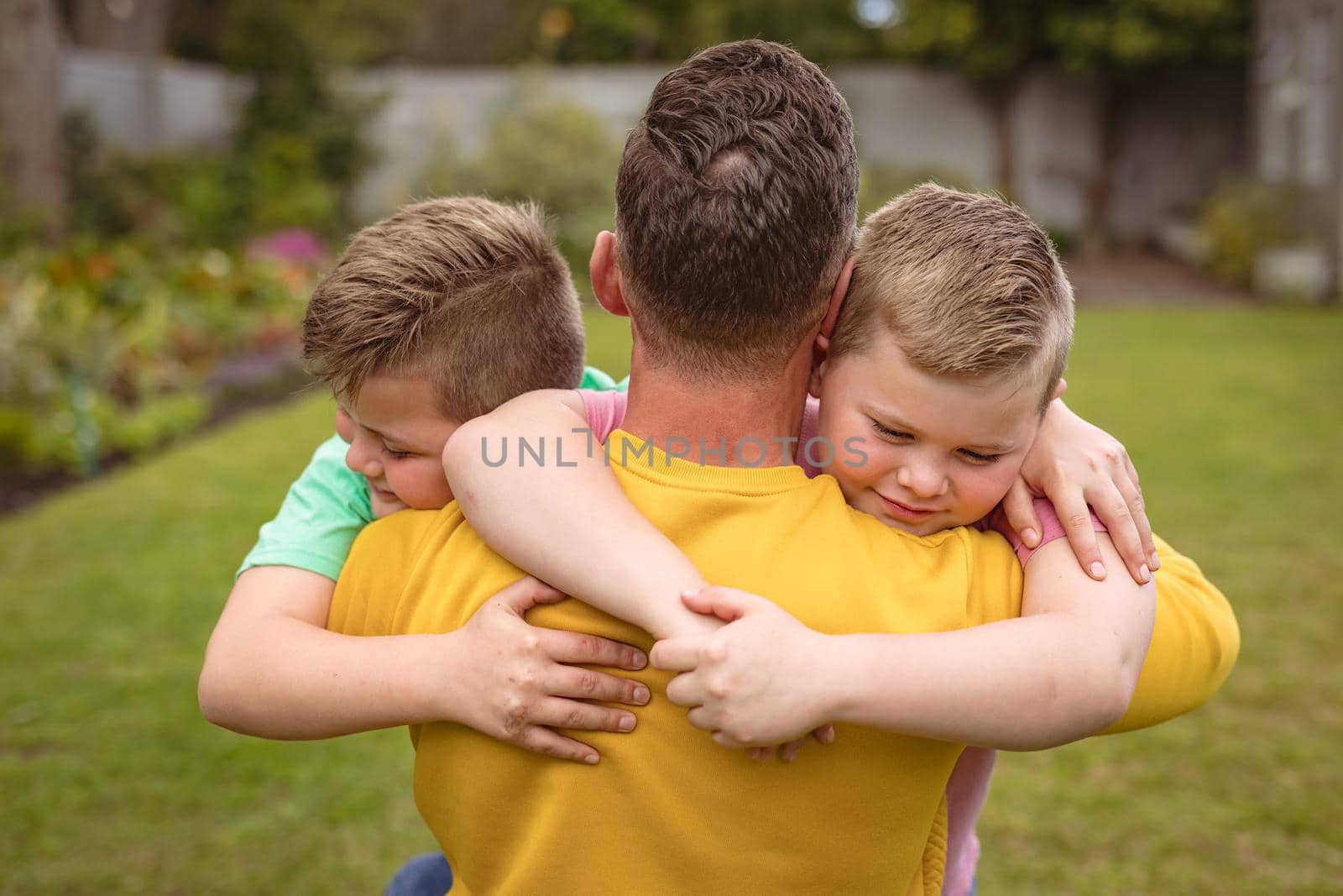 Close up view of caucasian father hugging his two sons in the garden. fatherhood and love concept