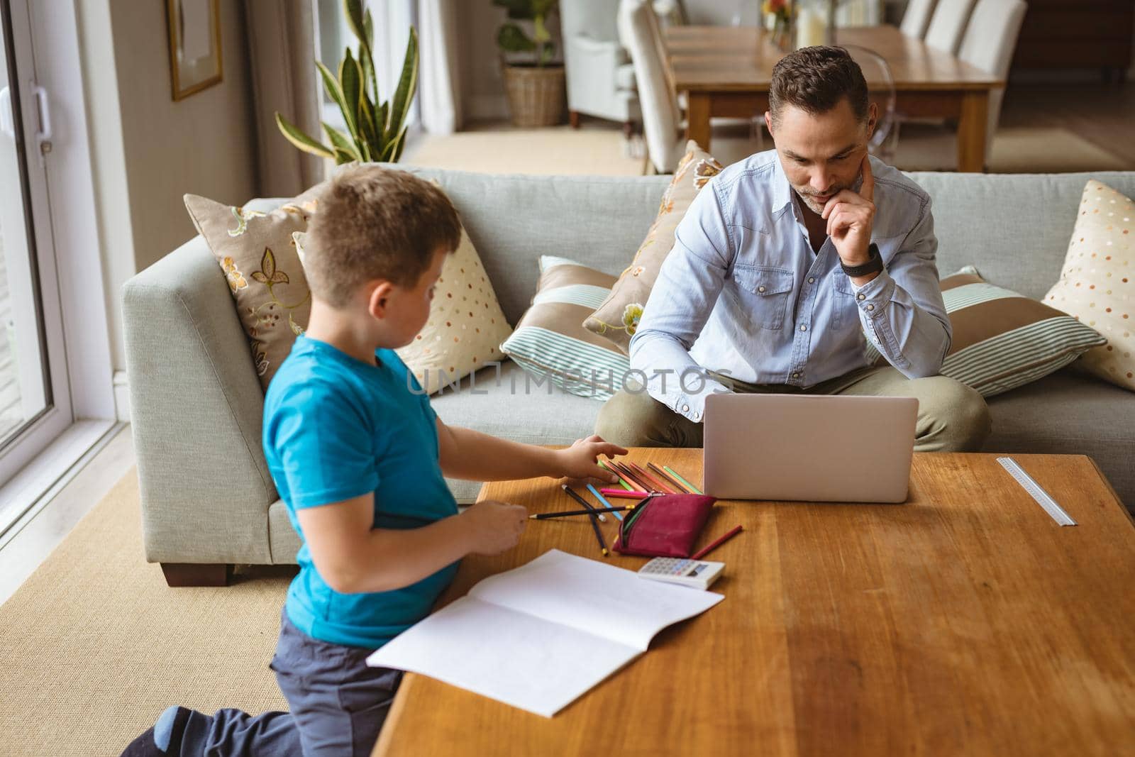 Caucasian father using laptop while son doing his homework at home. home schooling and working from home during coronavirus covid-19 pandemic concept