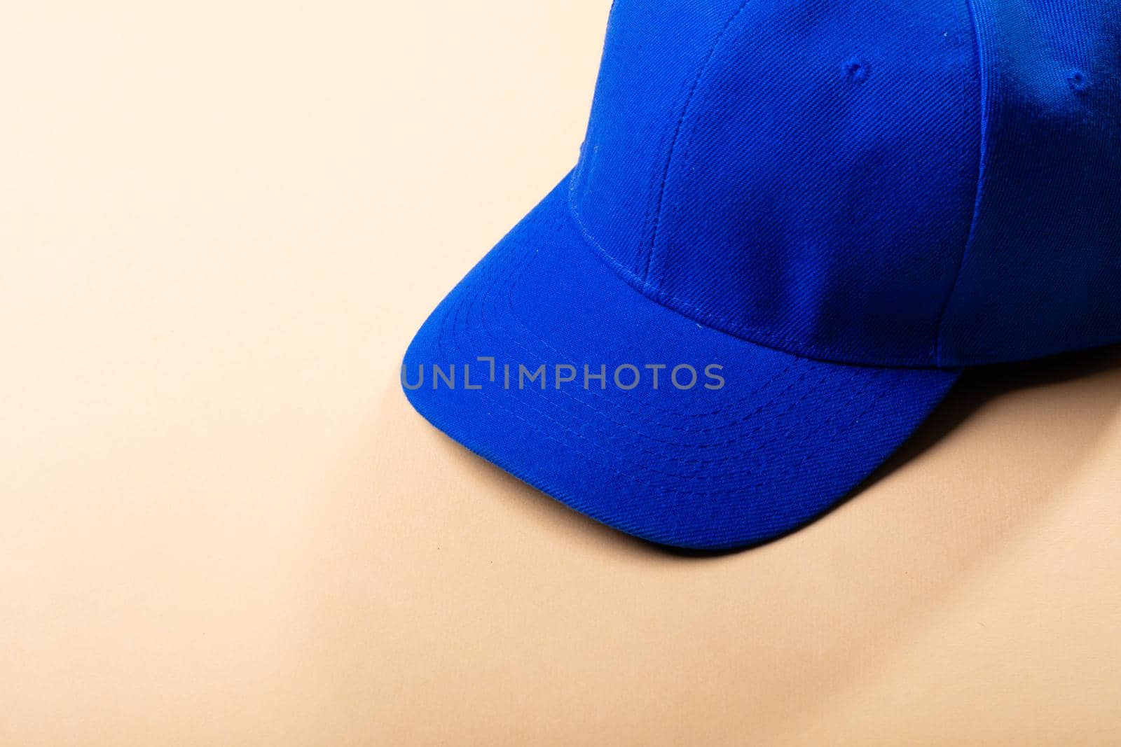 Composition of traditional peaked blue baseball cap on pale brown background. fashion and accessories concept.