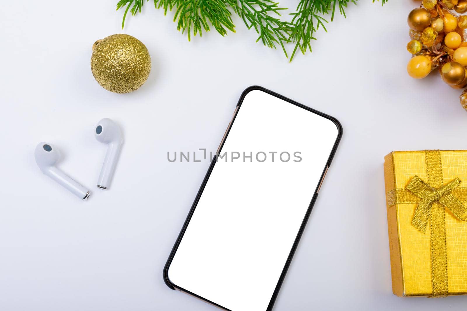 Composition of smartphone with copy space, wireless earphones and christmas decorations on white. christmas, tradition and celebration concept.