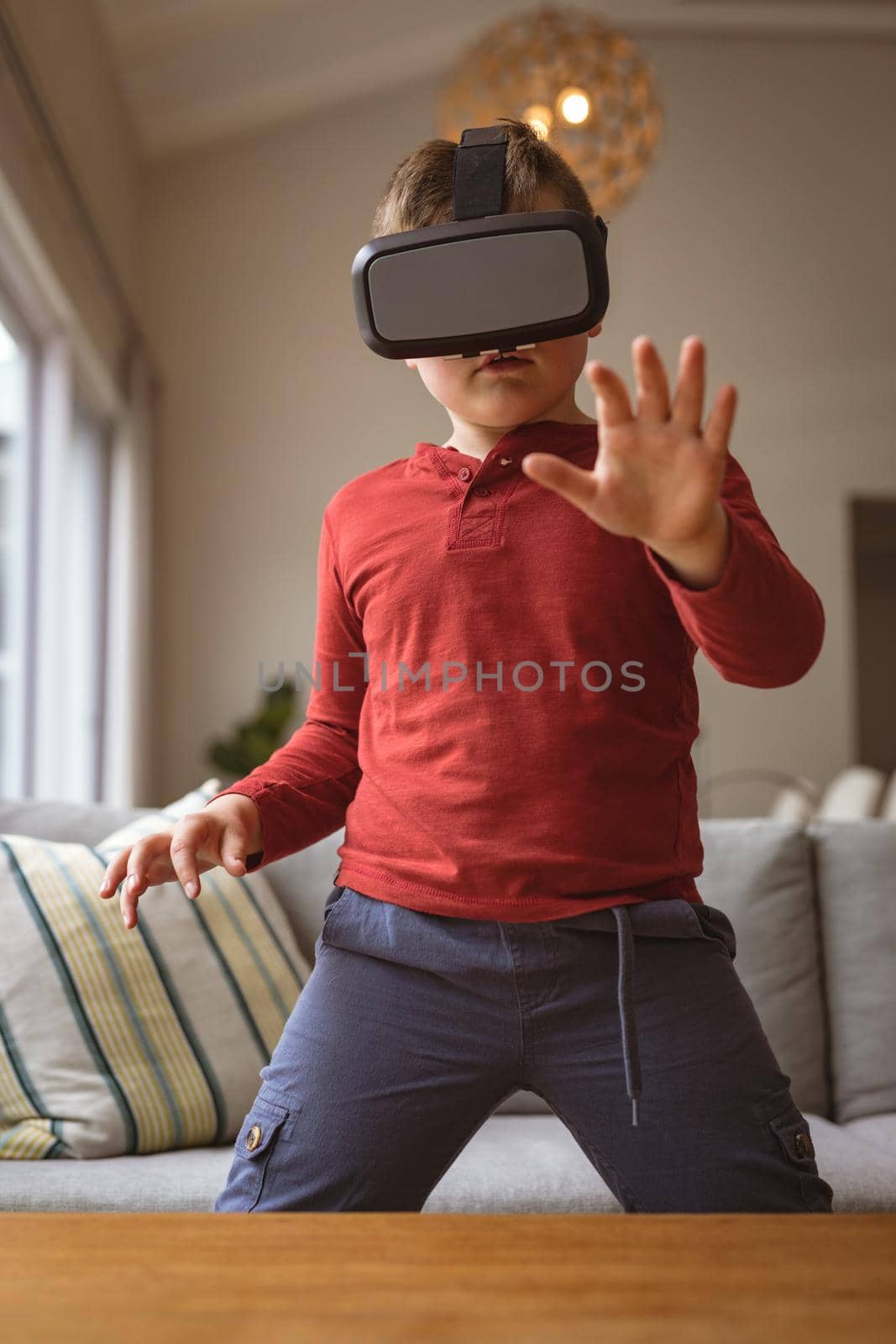 Caucasian boy wearing vr headset gesturing while sitting on the couch at home by Wavebreakmedia