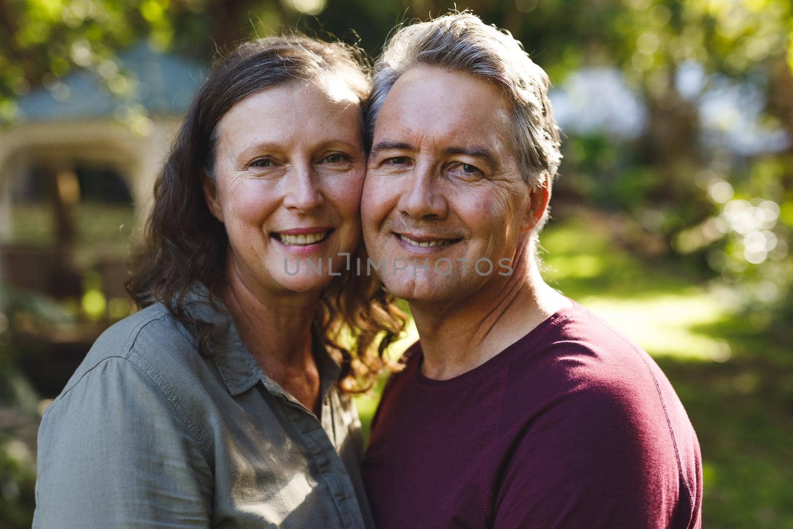 Portrait of happy senior caucasian couple embracing, looking to camera in sunny garden. retirement lifestyle, spending time at home.