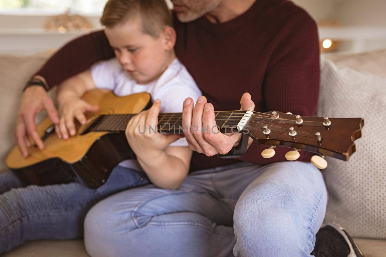 Mid section of caucasian father teaching his son to play guitar sitting on the couch at home by Wavebreakmedia