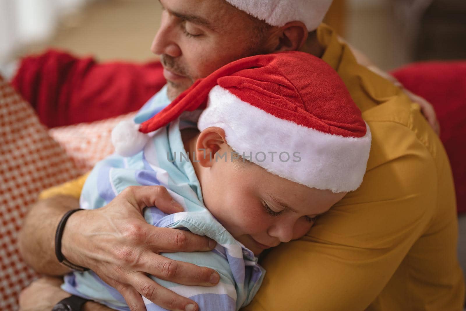 Caucasian father and son hugging each other sitting on the couch at home during christmas by Wavebreakmedia