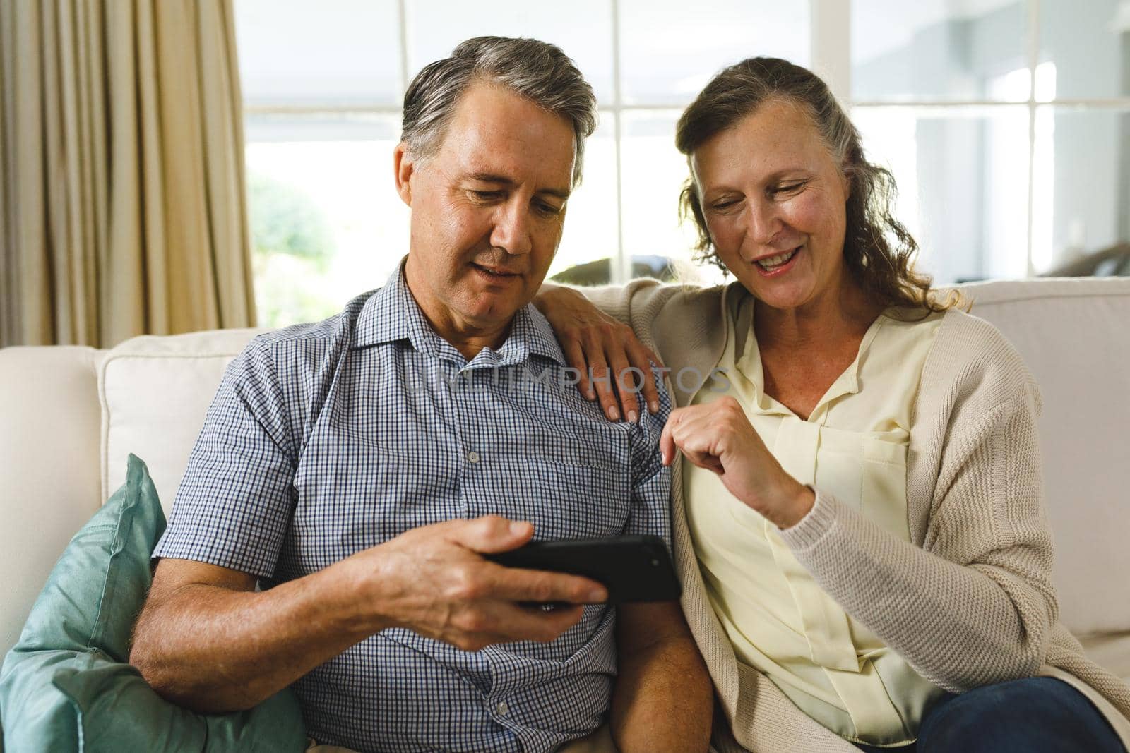 Happy senior caucasian couple in living room, sitting on sofa, using smartphone by Wavebreakmedia