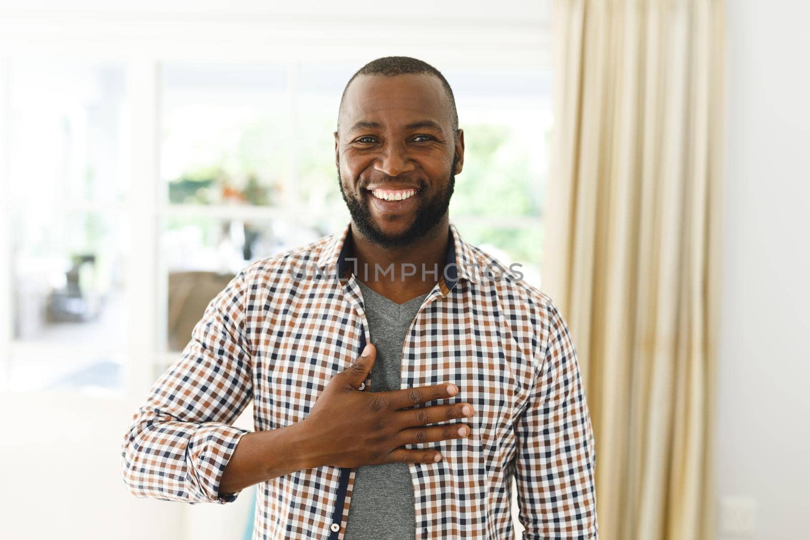 Portrait of african american man smiling and looking at camera in living room talking sign language by Wavebreakmedia