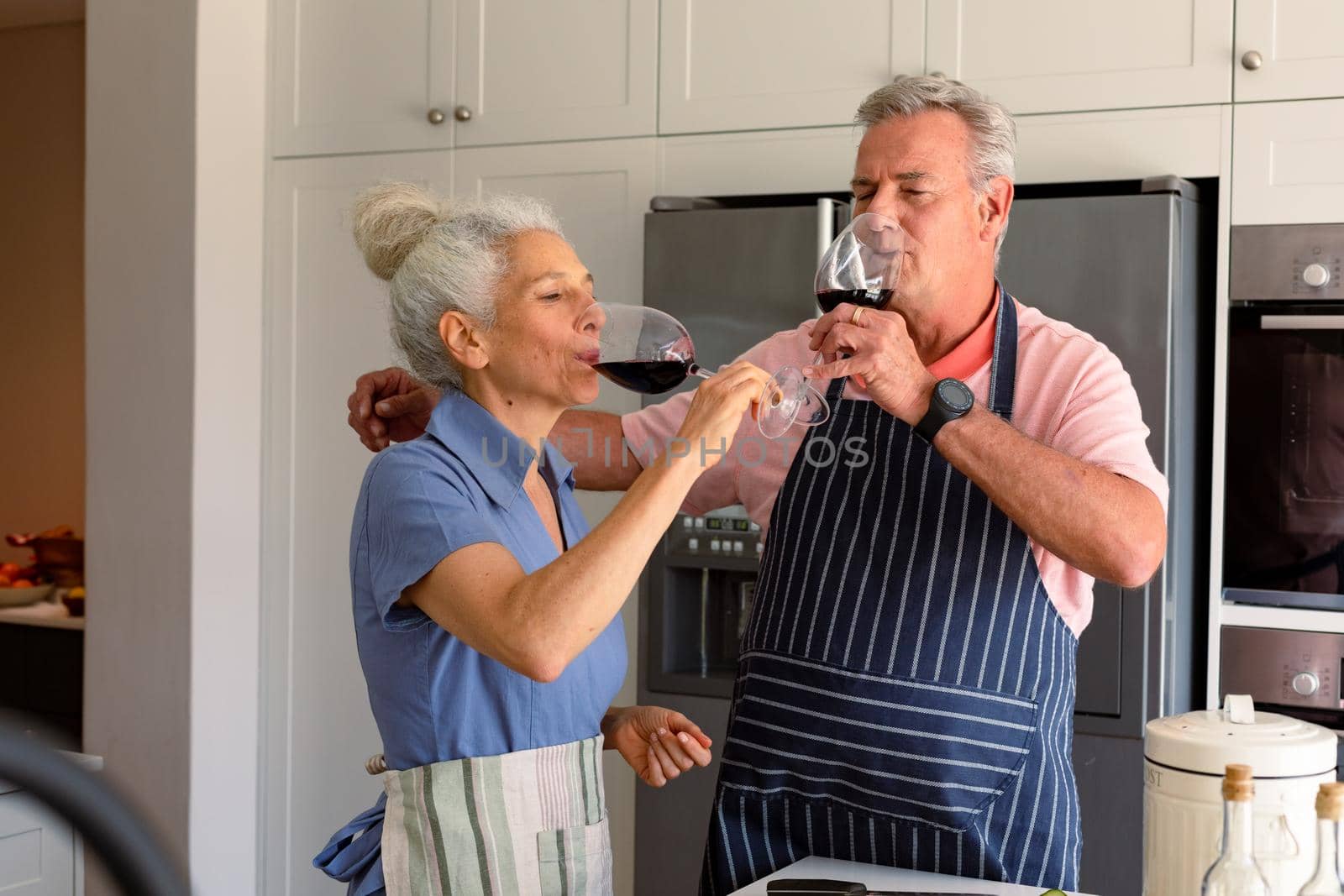 Caucasian senior couple standing in kitchen, drinking wine and preparing meal together. healthy retirement lifestyle at home.
