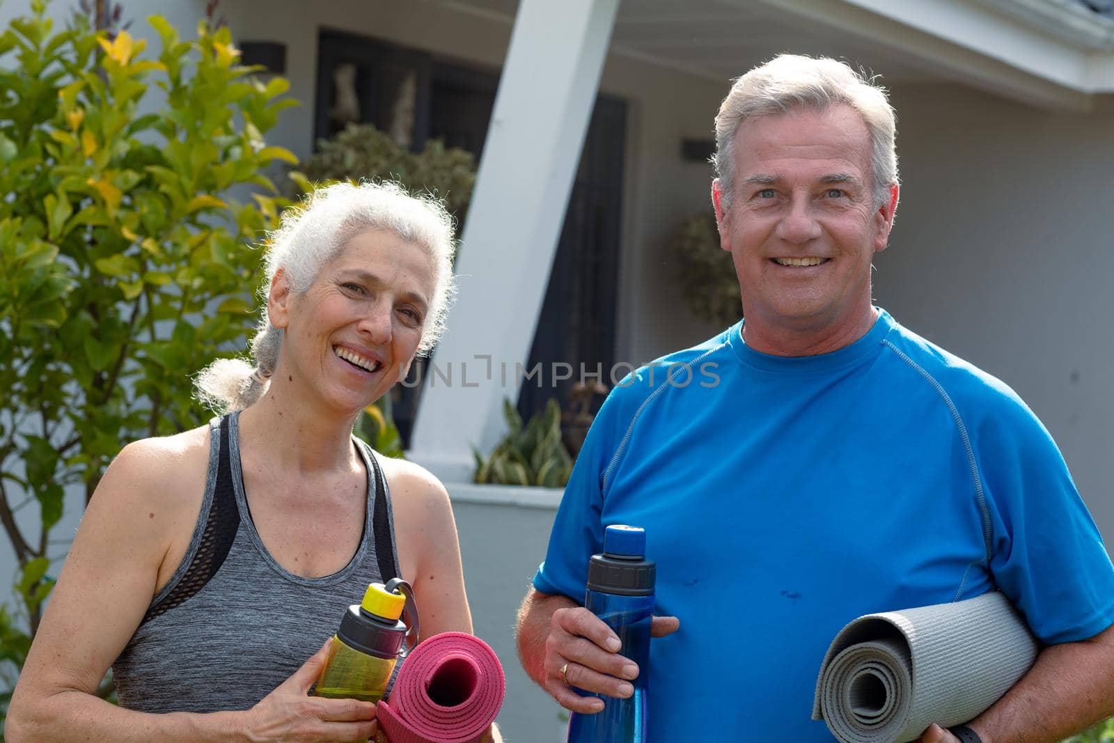 Happy caucasian senior couple holding yoga mats and looking at camera. active and healthy retirement lifestyle at home and garden.