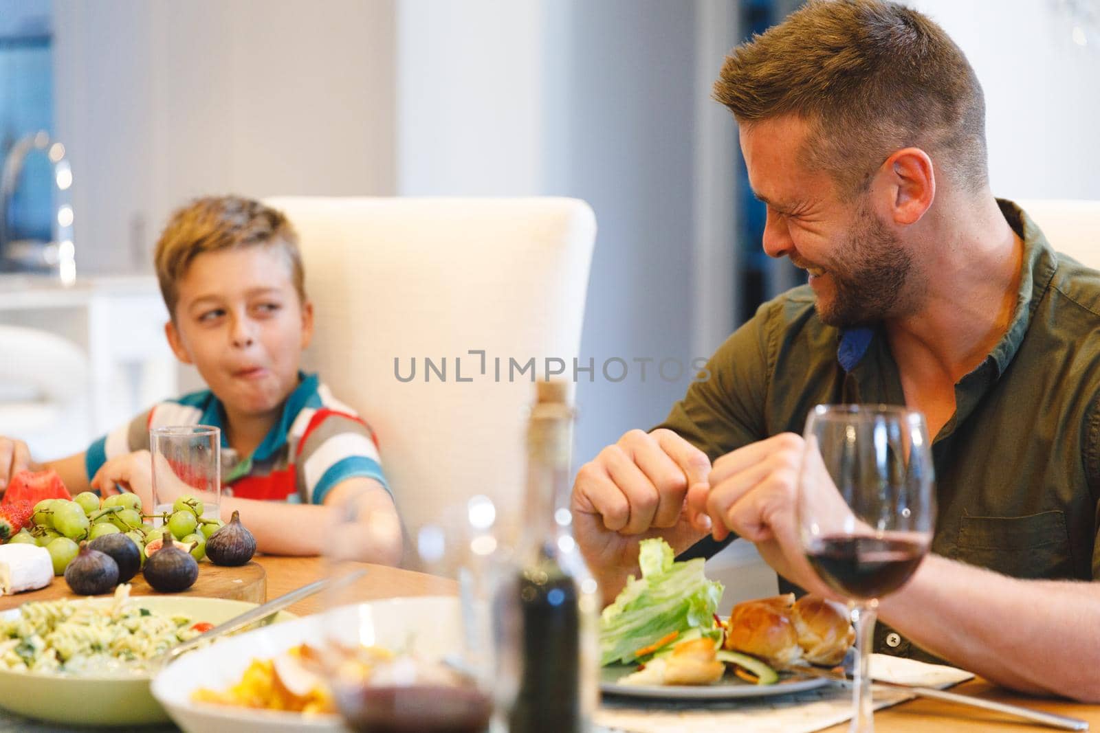 Happy caucasian father with son sitting at table and having dinner. family spending time together at home.