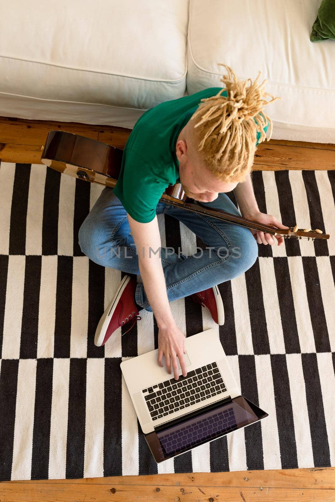 Albino african american man in the living room playing guitar and using laptop by Wavebreakmedia