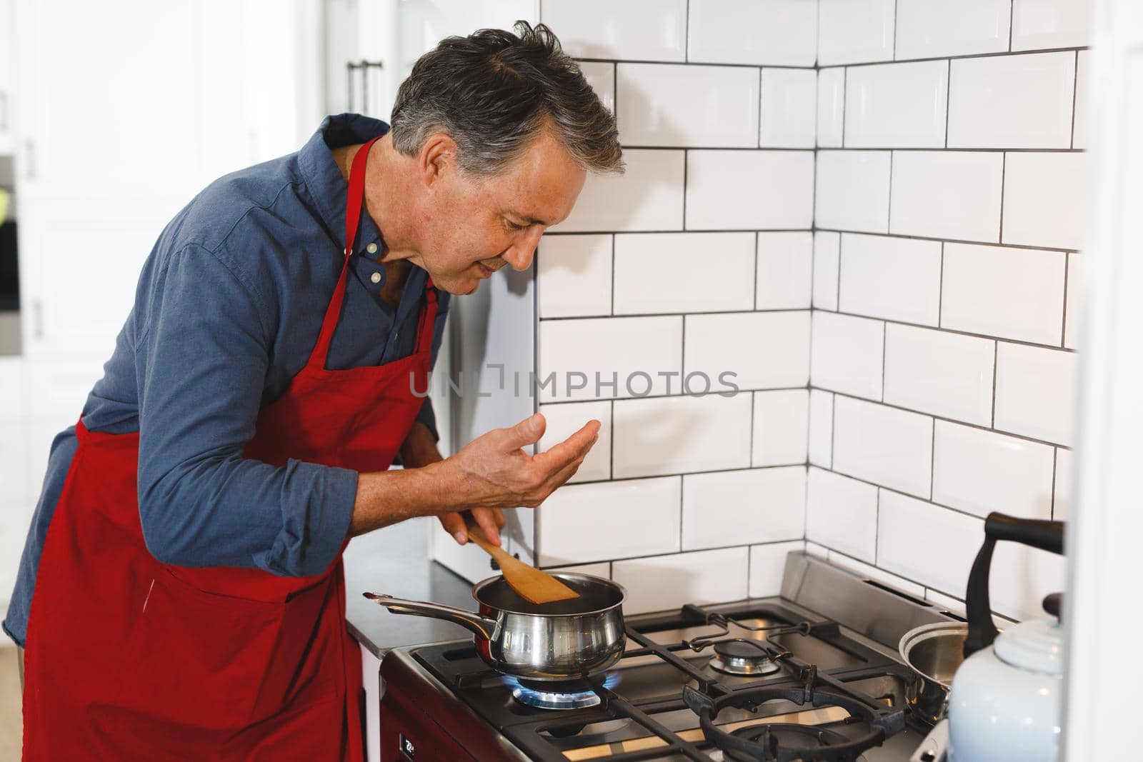 Happy senior caucasian man wearing apron in kitchen cooking. retirement lifestyle, spending time at home.