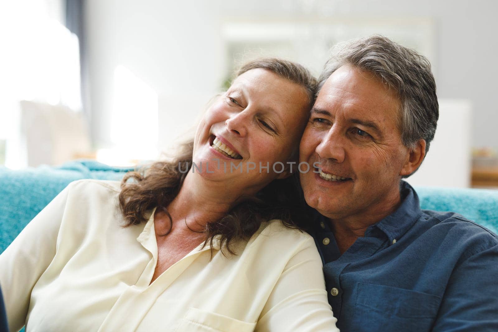 Happy senior caucasian couple in living room sitting on sofa, embracing. retirement lifestyle, spending time at home.