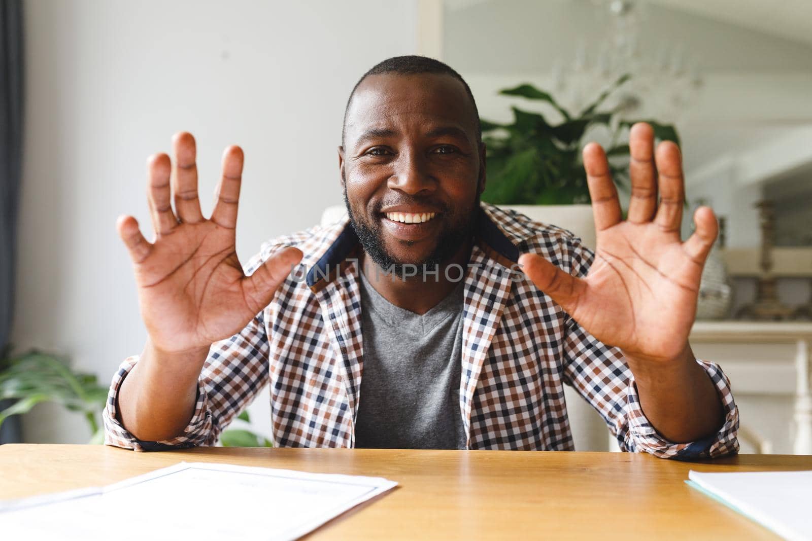 Smiling african american man sitting at table gesturing in dining room, making video call by Wavebreakmedia