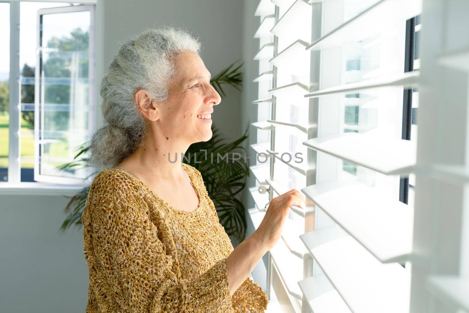 Smiling caucasian senior woman standing at window, looking into distance by Wavebreakmedia