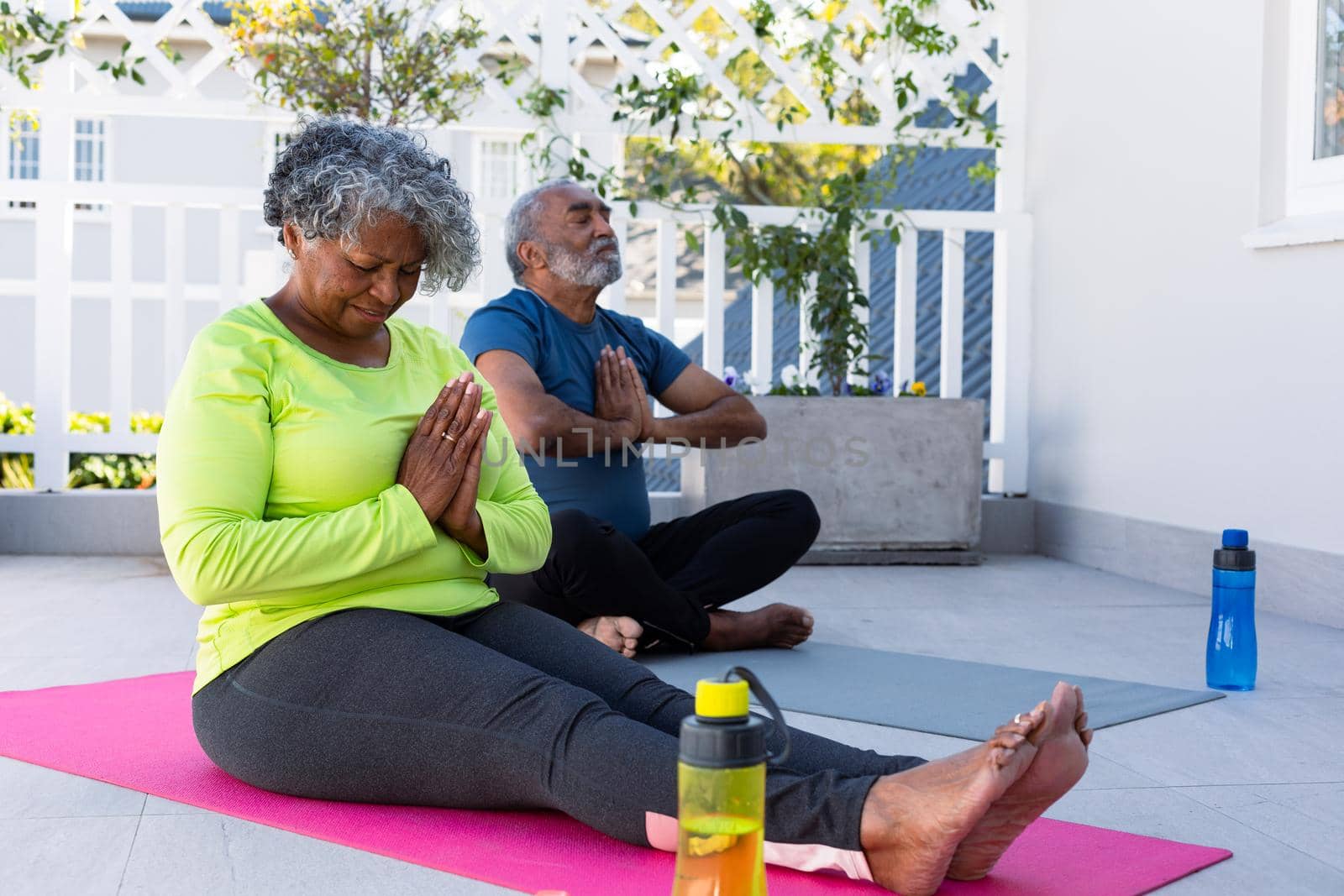 Focused african american senior couple practicing yoga on mat in garden. active and healthy retirement lifestyle at home.