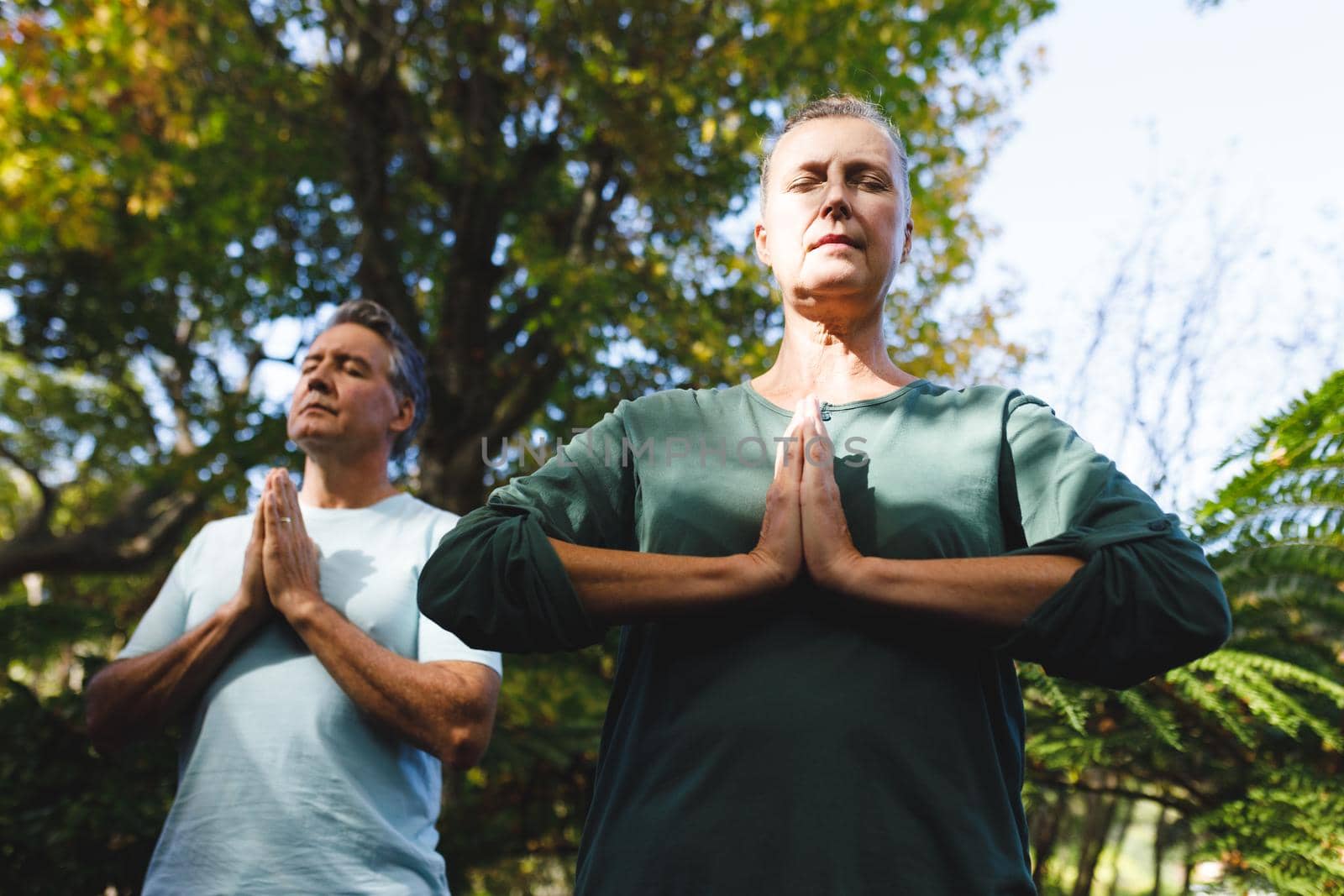 Peaceful senior caucasian couple practicing yoga, meditating in sunny garden. healthy retirement lifestyle, spending time at home.