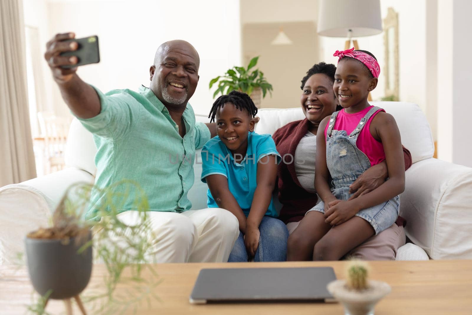 African american grandfather and grandmother on couch smiling with grandchildren taking selfie by Wavebreakmedia