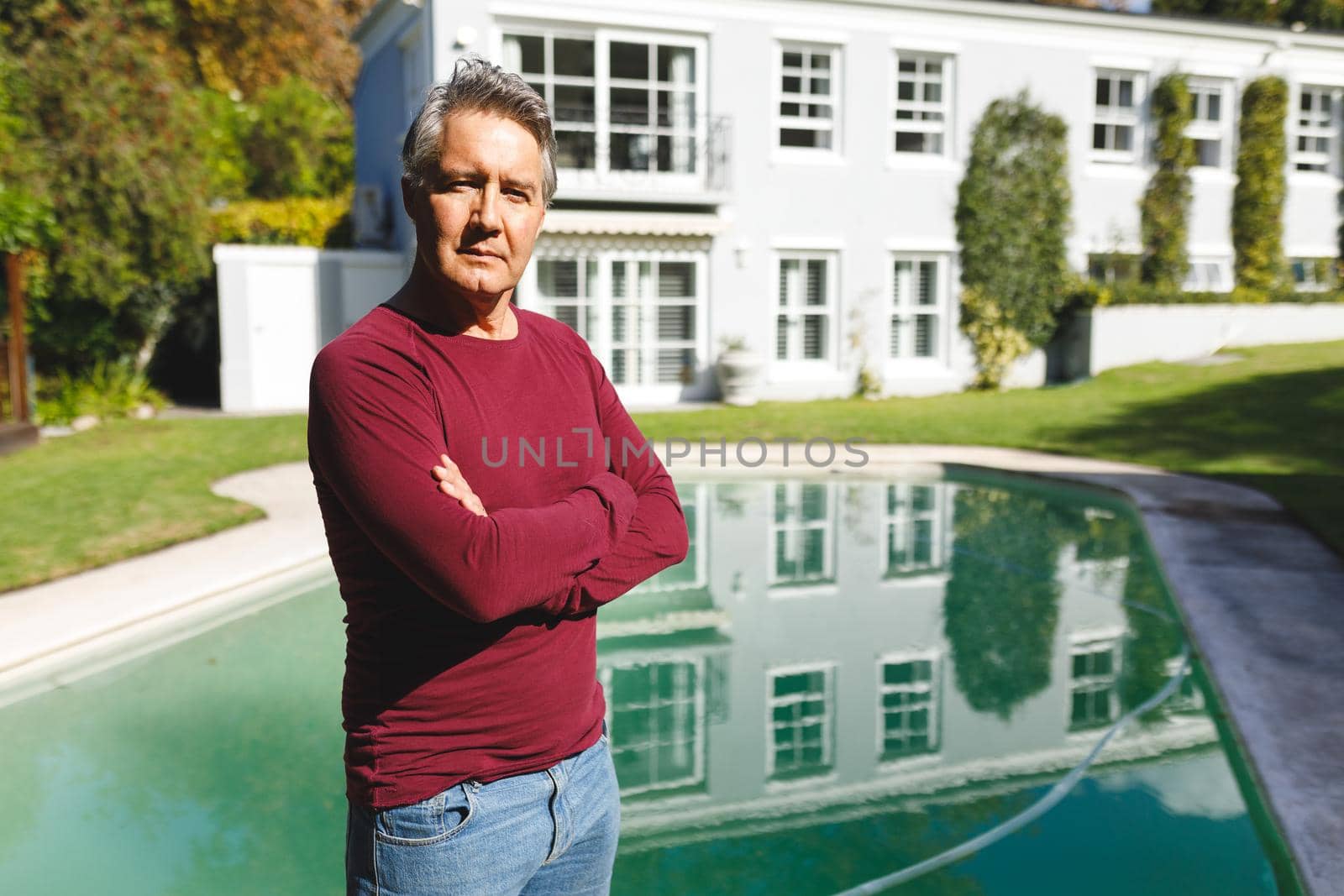 Portrait of successful senior caucasian man with arms crossed, looking to camera in sunny garden. luxury retirement lifestyle, spending time at home.