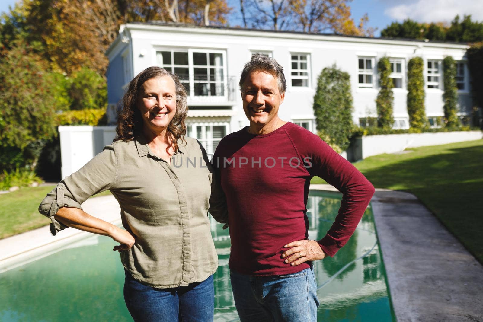 Portrait of happy senior caucasian couple embracing, looking to camera in sunny garden. luxury retirement lifestyle, spending time at home.