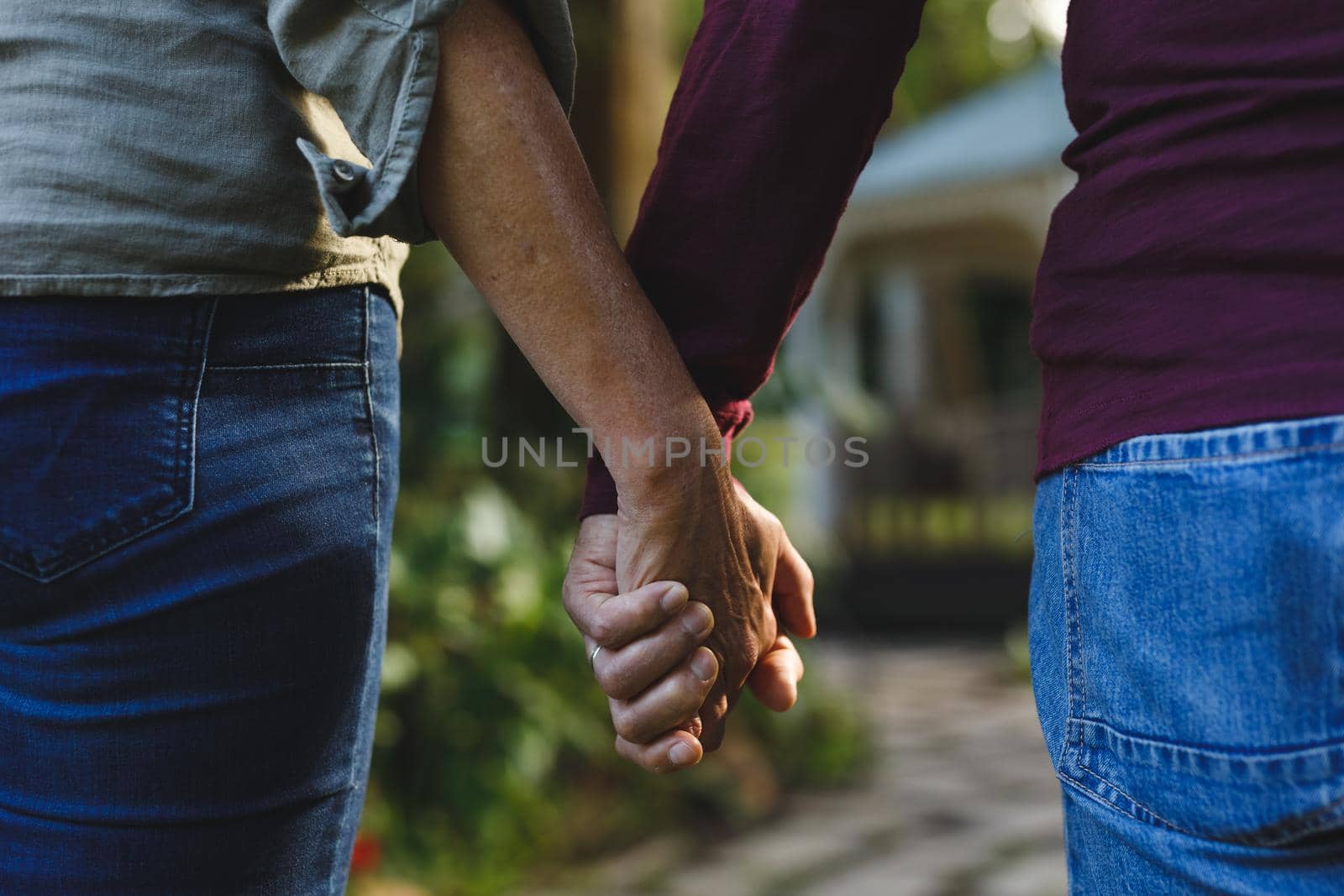 Midsection of senior caucasian couple holding hands walking in garden. retirement lifestyle, spending time at home.