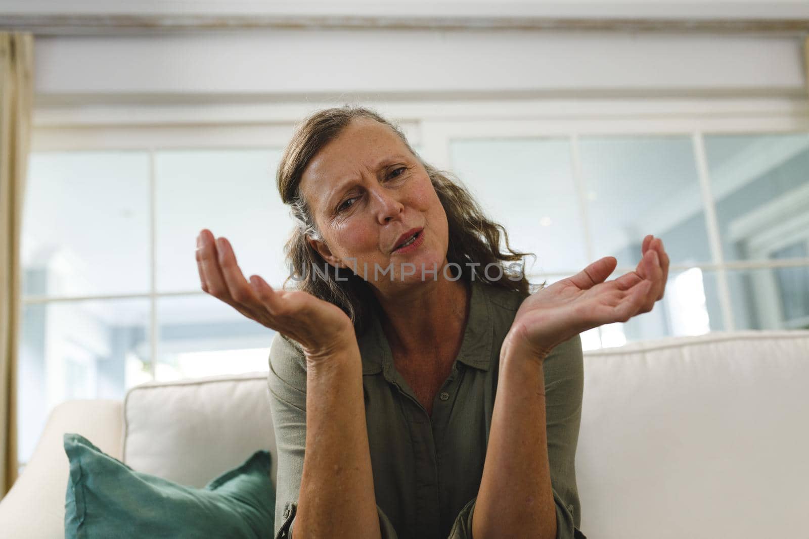 Senior caucasian woman in living room, sitting on sofa, talking and gesturing during video call. retirement lifestyle, spending time at home with technology.