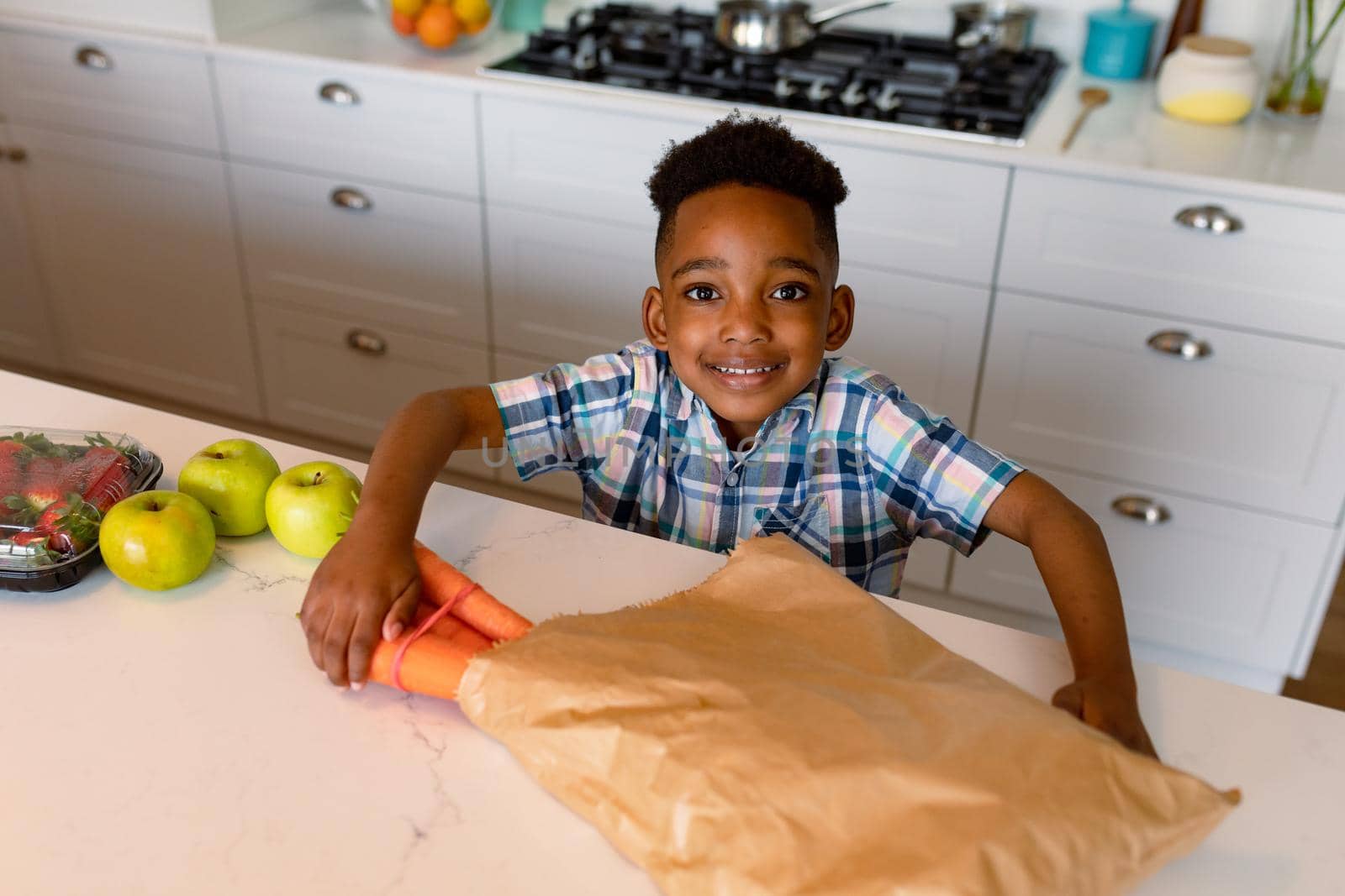 Happy african american boy unpacking groceries in kitchen. childhood, leisure and spending time at home.