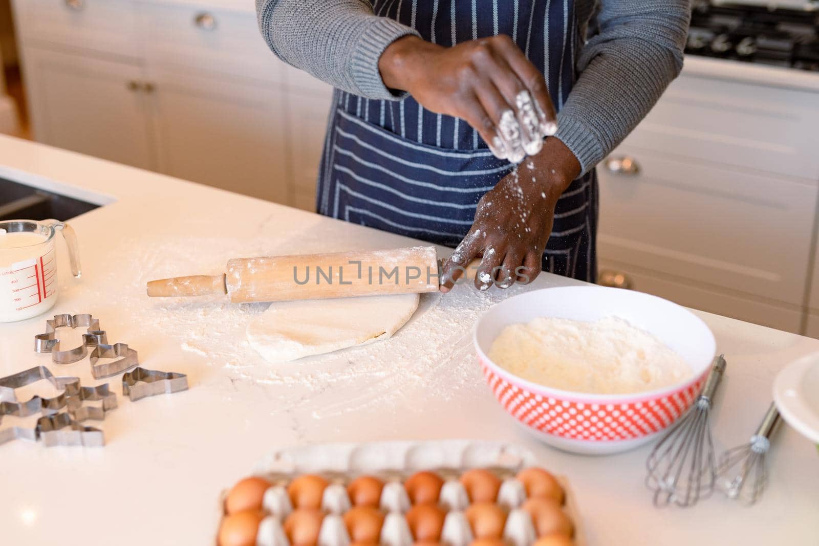 Midsection of african american man wearing apron, baking in kitchen. cooking and baking, spending time at home.