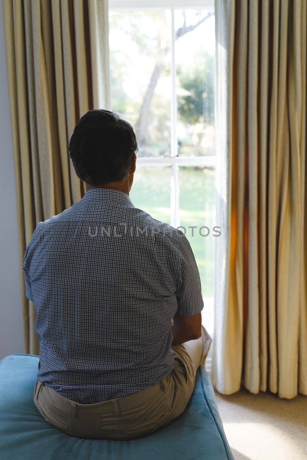 Thoughtful senior caucasian man sitting on sofa and looking through window by Wavebreakmedia