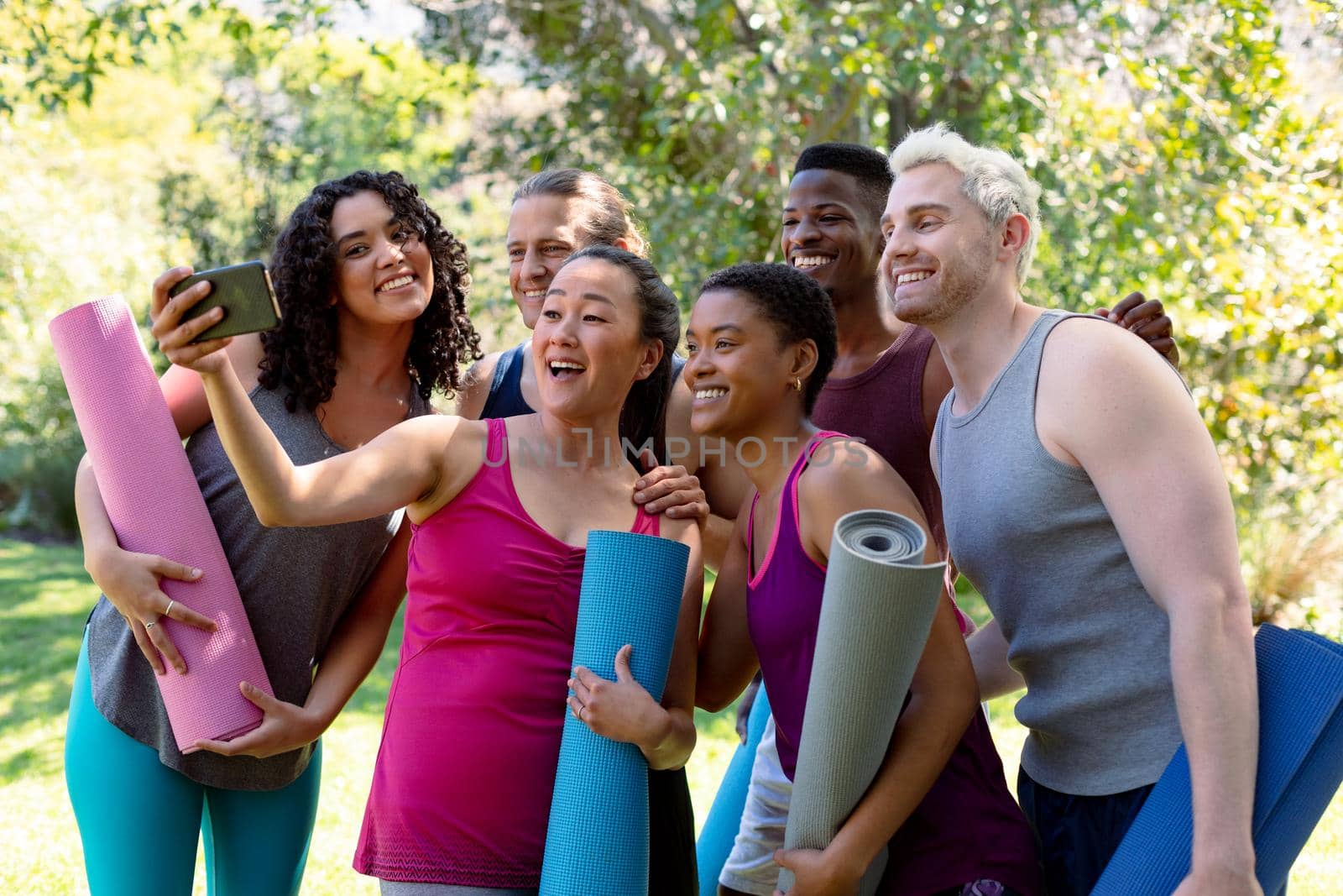 Group of happy fit diverse female and male friends holding yoga mats and taking selfie by Wavebreakmedia