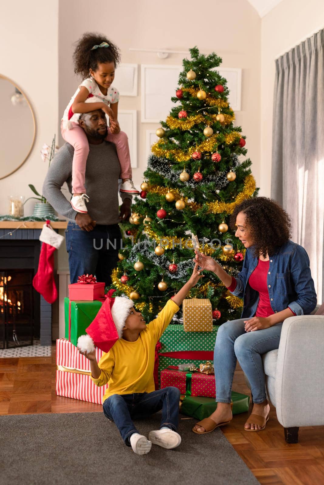 Happy african american father wearing santa hat and daughter decorating christmas tree. christmas, festivity and tradition at home.