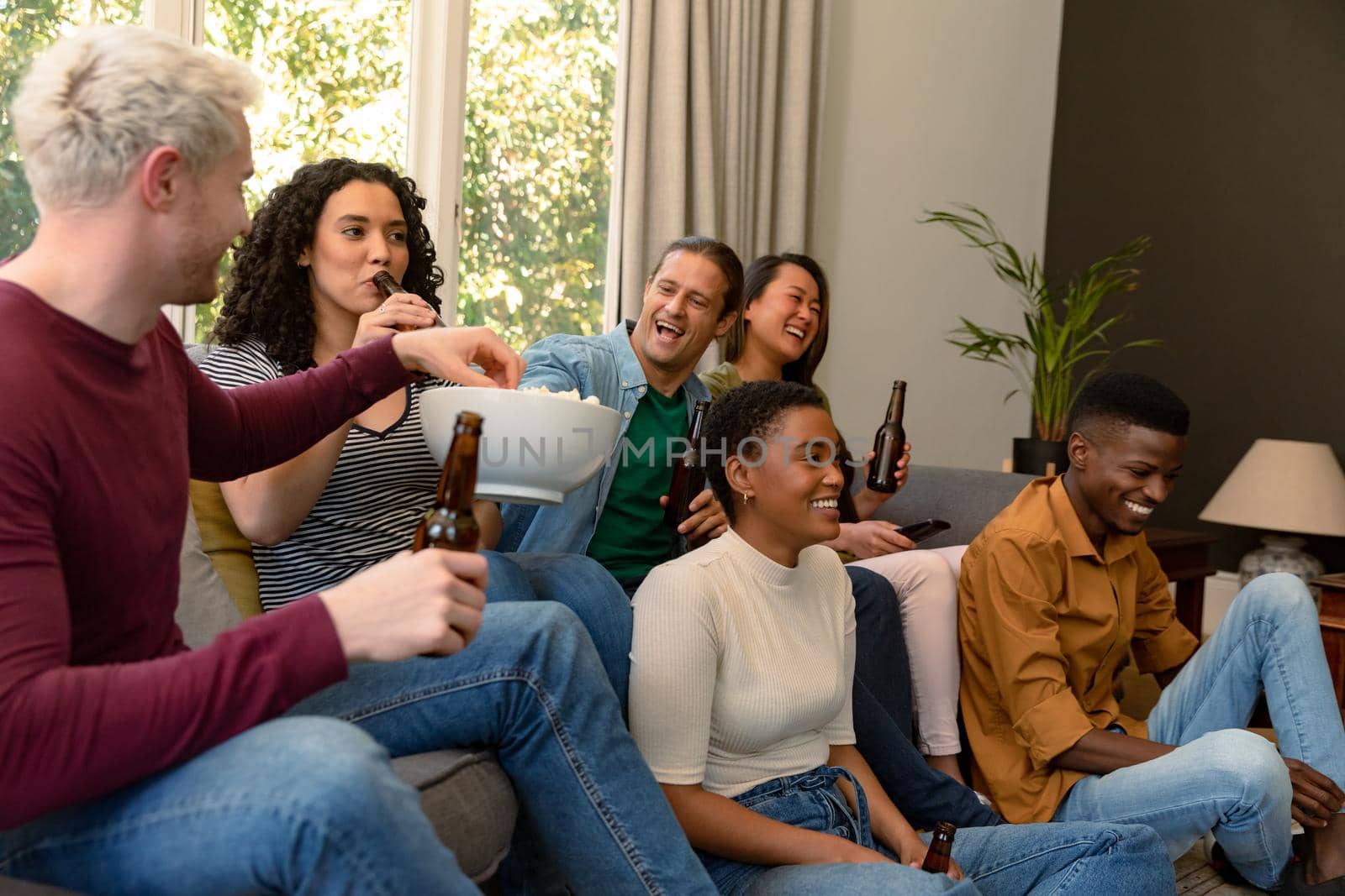 Group of happy diverse female and male friends watching tv and drinking beer together at home by Wavebreakmedia