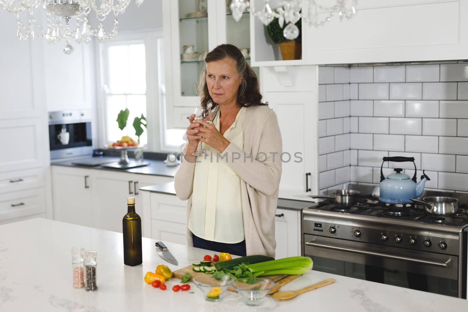Senior caucasian woman in modern kitchen, holding glass of wine. retirement lifestyle, spending time at home.