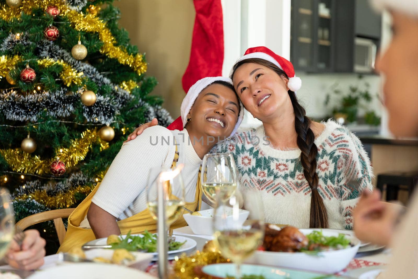 Happy diverse female friends in santa hats embracing, celebrating christmas with friends at home. christmas festivities, celebrating at home with friends.