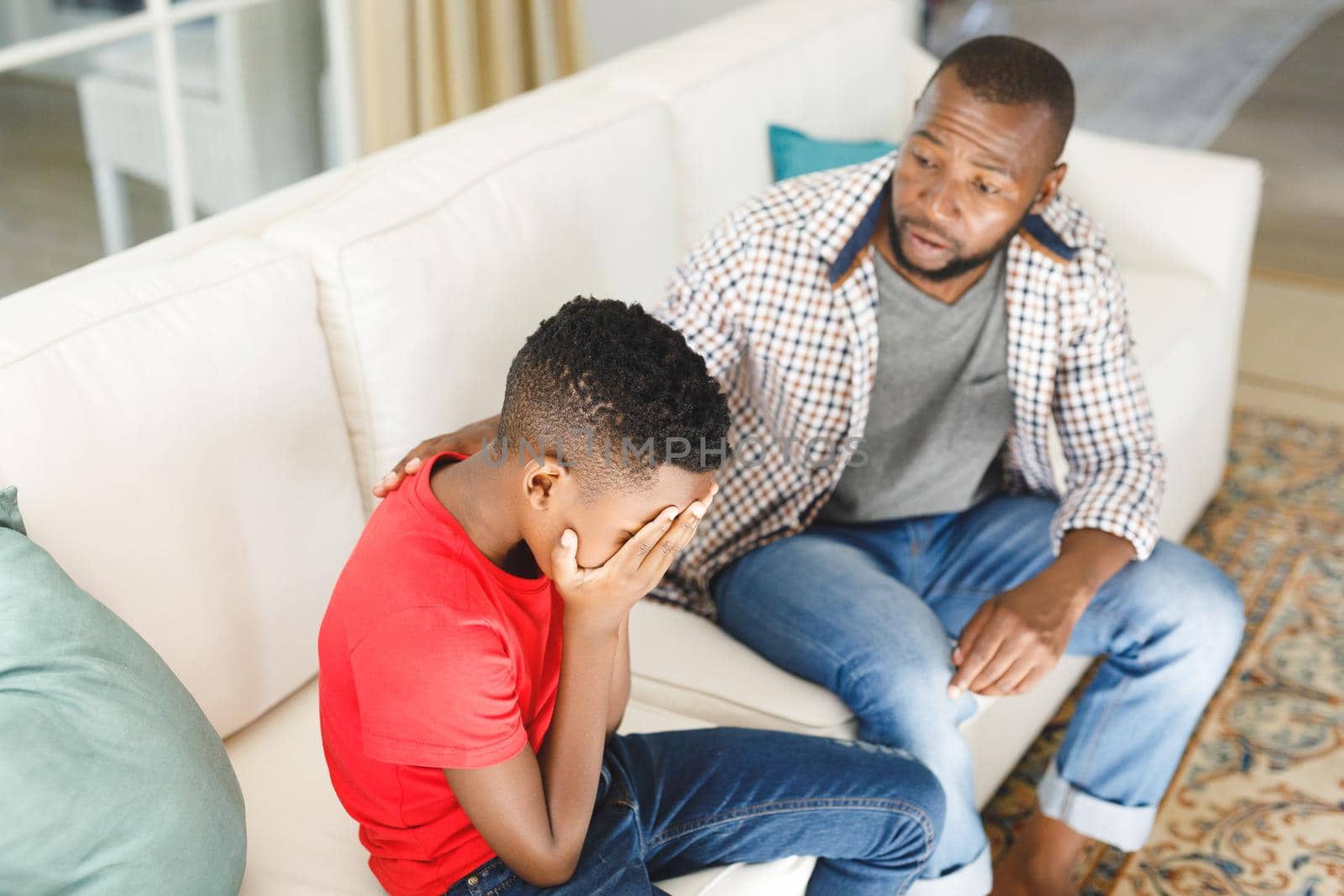Sad african american son sitting on couch covering face listening to father talking in living room. family spending time at home, father son relationship.