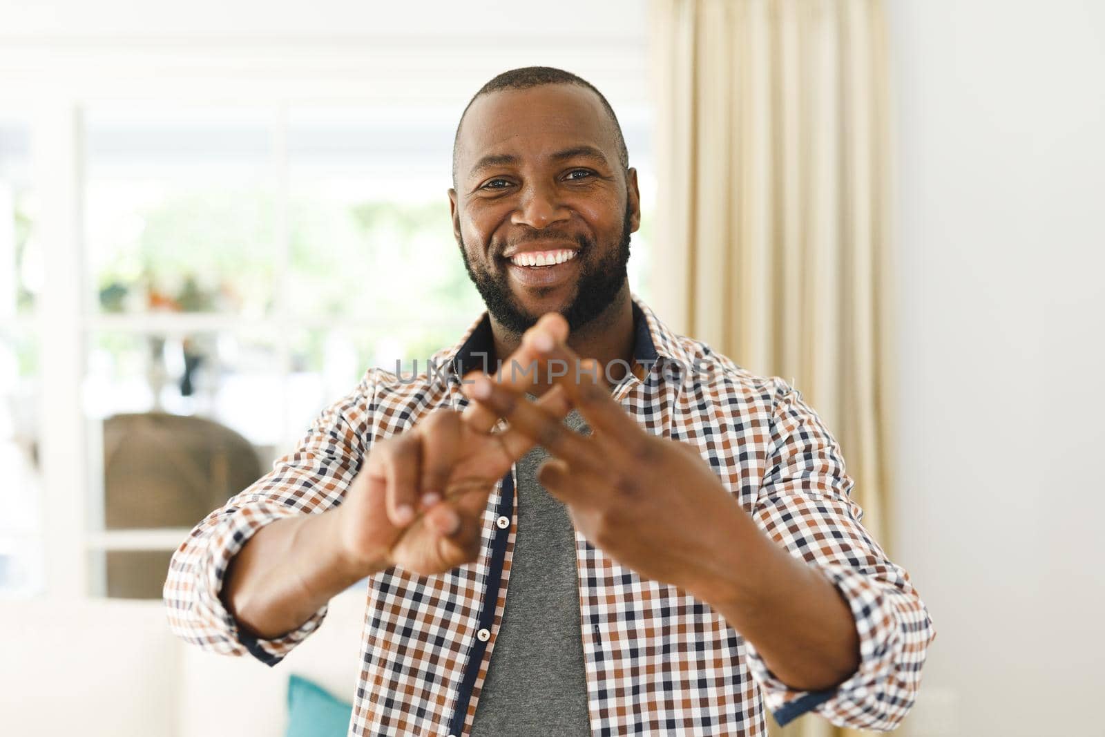 Portrait of african american man smiling and looking at camera in living room talking sign language by Wavebreakmedia