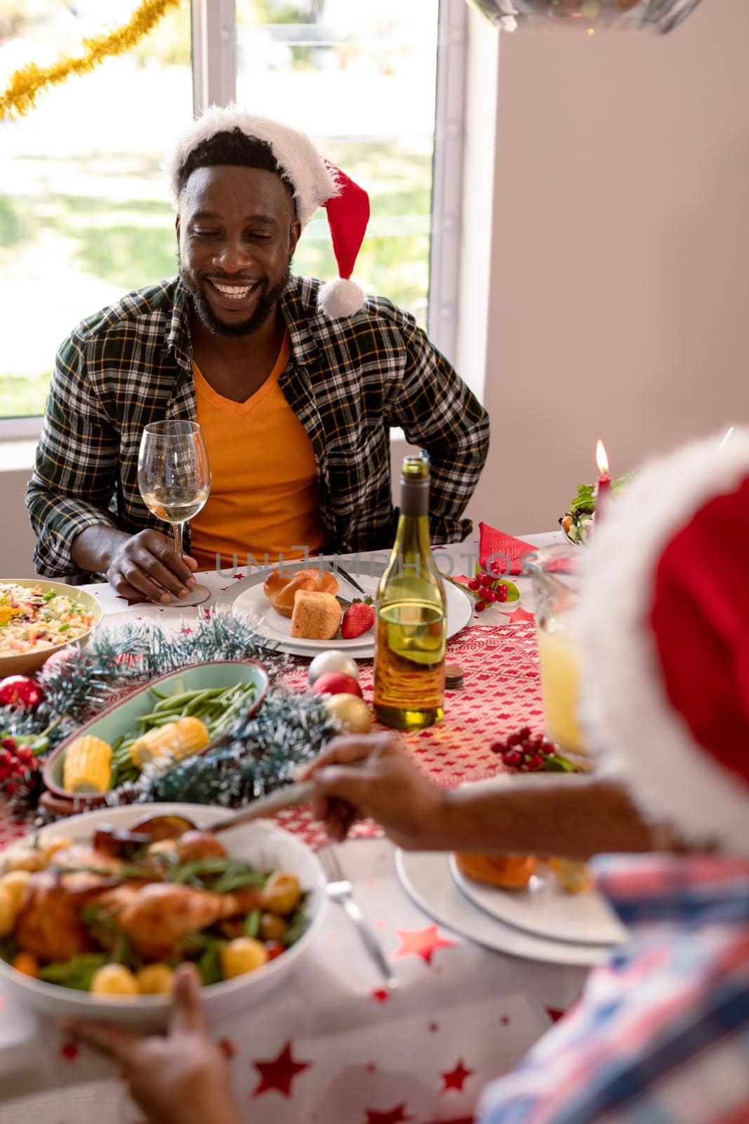 Happy african american man wearing santa hat holding glass at christmas table by Wavebreakmedia