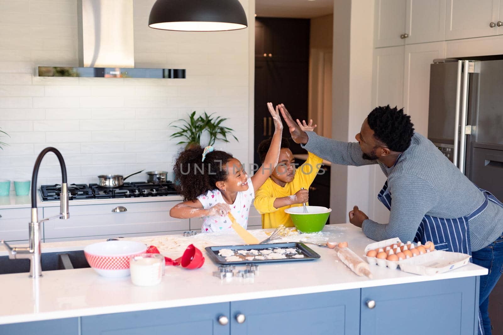 Happy african american father and siblings baking together in kitchen, giving high five. baking and cooking, family time, having fun together at home.