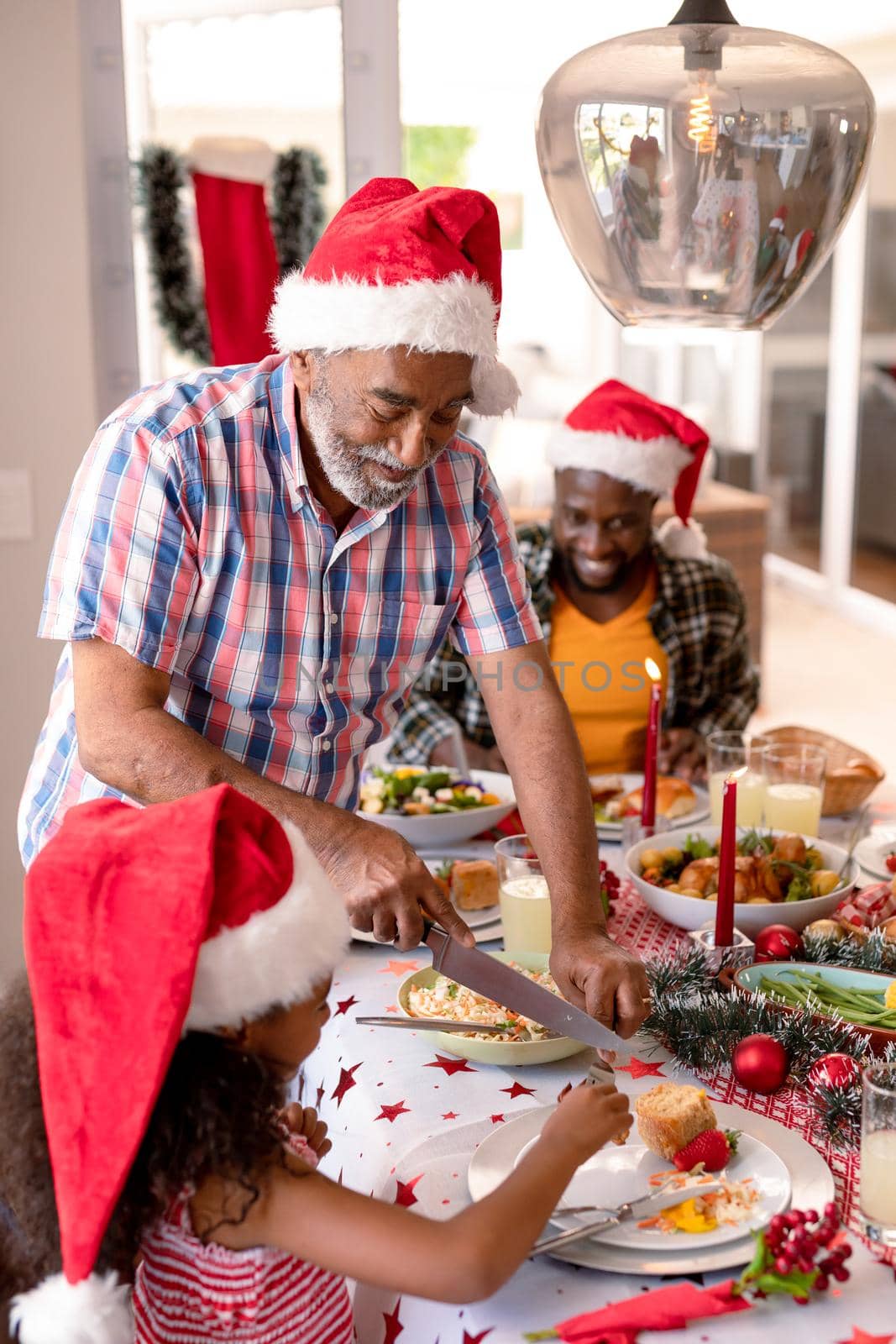 Happy african american grandfather cutting granddaughter dish. family christmas time and festivity together at home.