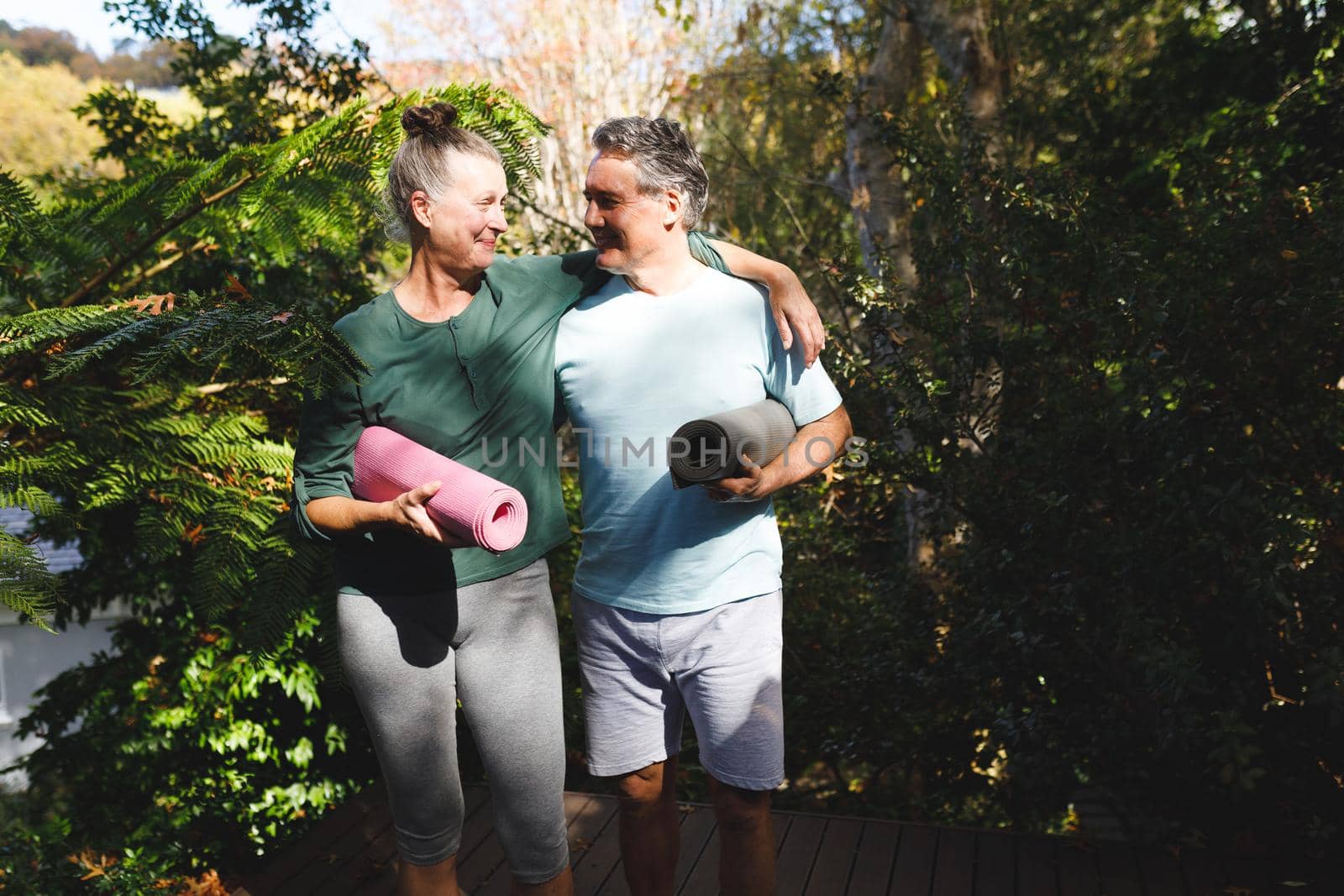Happy senior caucasian couple practicing yoga, holding yoga mats in sunny garden by Wavebreakmedia