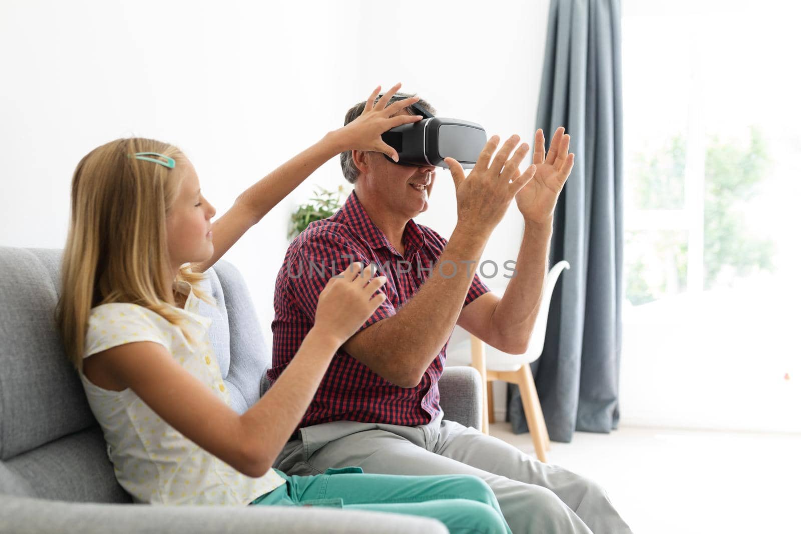 Caucasian granddaughter sitting on couch beside grandfather adjusting his vr headset by Wavebreakmedia