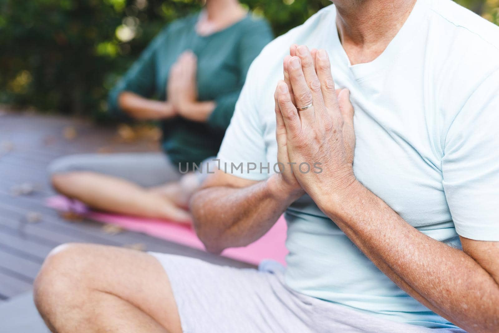Midsection of senior caucasian couple practicing yoga, meditating in sunny garden. healthy retirement lifestyle, spending time at home.