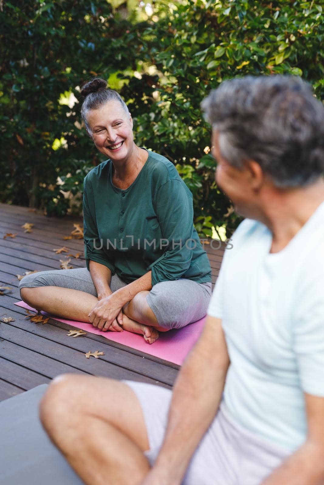 Happy senior caucasian couple practicing yoga, talking in sunny garden. healthy retirement lifestyle, spending time at home.
