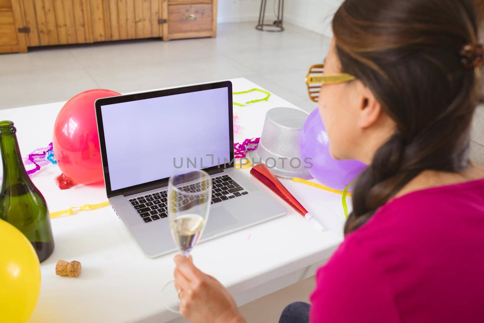 Happy asian woman with champagne making new year's eve video call on laptop with copy space. o celebrating at home with communication technology.