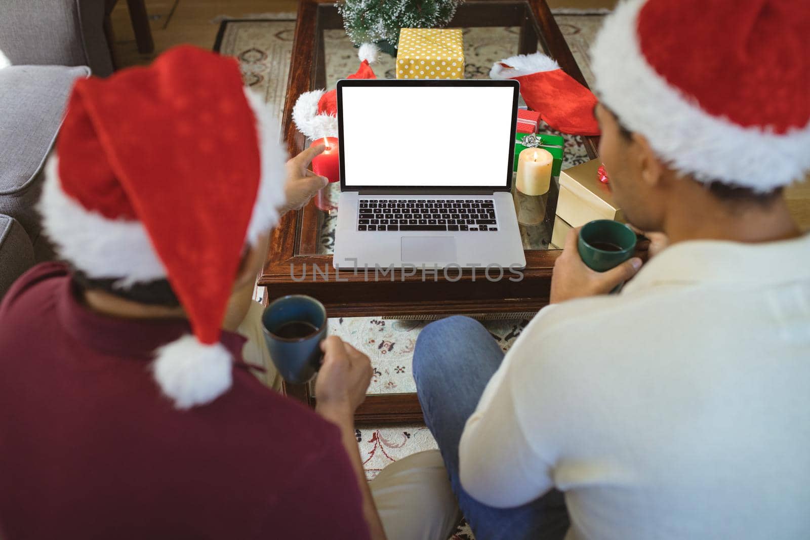 Biracial adult son and senior father in santa hats making laptop christmas video call. christmas, festivity and communication technology.
