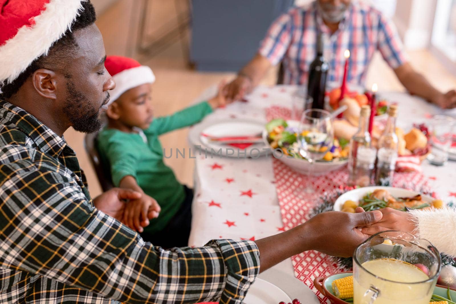 Happy multi generation family wearing santa hats, praying together, having christmas meal by Wavebreakmedia