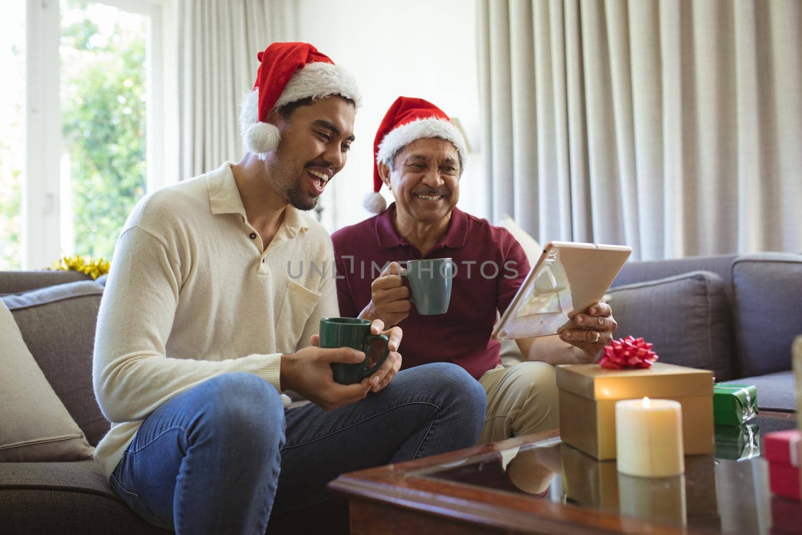 Happy biracial adult son and senior father in santa hats making laptop christmas video call by Wavebreakmedia